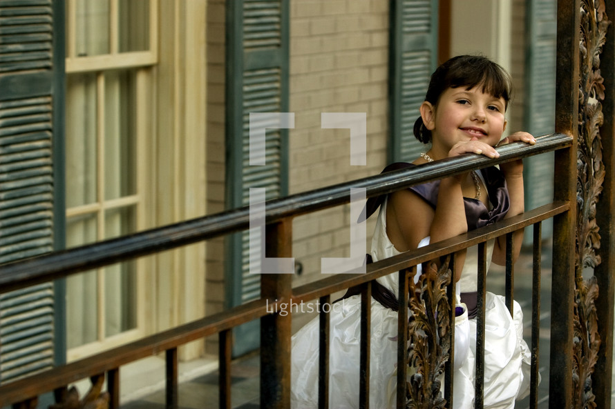 Girl leaning on rail in front of windows.