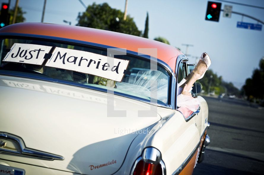 Bride and groom in classic car with "Just Married" in back window brides foot hanging out window