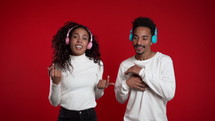 Young african american couple dancing with headphones isolated on red background studio. Party, happiness, music concept. Slow motion