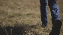 a close up of a young man's shoes and the ground as he is walking through a field in the mountains