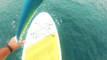 First person on a SUP board on sea. A man uses an oar to sail through the waves.