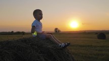 Countryside. Pretty boy lying on a haystack. Happy childhood. Adorable little child in a august field with haystacks. Summer holidays, ecology and health.
