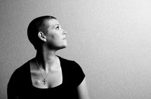 profile of a woman with shaved head wearing a cross necklace