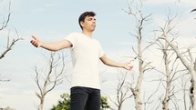 young man standing outdoors with outstretched arms 