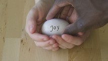 cupped hands holding an egg with the word joy on it 