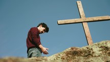 a man praying on a mountaintop next to a cross 