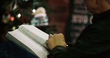 a man reading a Bible in front of a Christmas tree