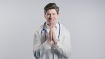 Mature 30s aged physician man in white medical coat form praying with hands on white background. Begs someone satisfy desires, help with, prays for luck. High quality 4k footage