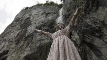 a woman with hands raised standing under a waterfall 