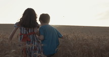 Boy and girl running in a golden wheat field together towards the sunset