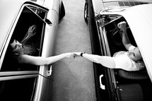man and woman holding hands through car windows