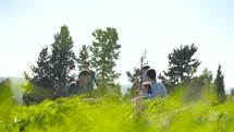 A family with 4 children having a picnic outdoors on a green hill in the sun.