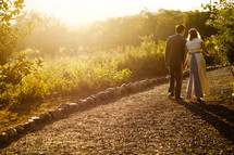bride and groom walking down a dirt road holding hands fall at sunset. Man wife