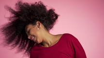 Beautiful african american woman with afro hair having fun smiling and dancing in studio against pink background.