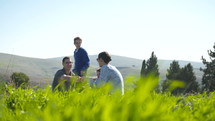 A family with 4 children having a picnic outdoors on a green hill in the sun.