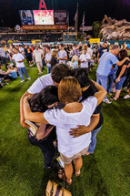 Family in a huddle on baseball field praying salvation crusade holding hugging love trust