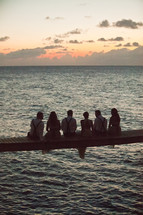 group of people sitting on bridge across ocean