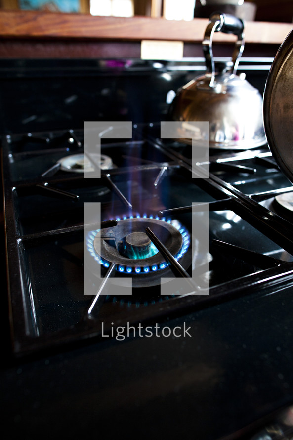 A gas stove top with one burner on, and a copper tea kettle.