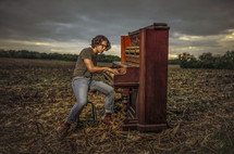 a man playing a piano in a plowed field 