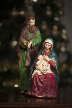 figurines of Mary, Joseph, and baby Jesus in front of a Christmas tree 