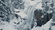 Beautiful, scenic waterfall nestled in the mountains with snow falling down