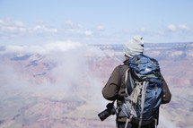 a man with a backpack and camera looking down at the canyon below 