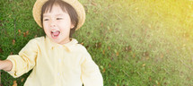 Happy Little Asian girl wearing straw hat and smile resting on green grass