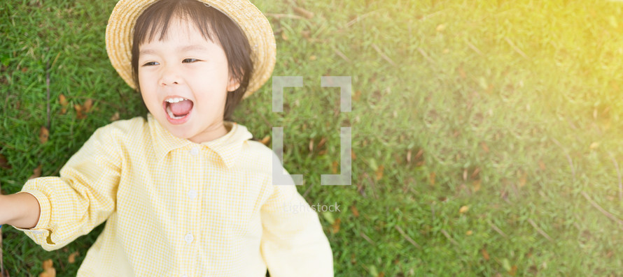 Happy Little Asian girl wearing straw hat and smile resting on green grass