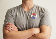 A man in a gray t-shirt wearing a button reading, "Vote."