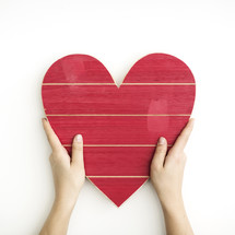 hands holding up a red wooden Valentine's Day heart 