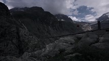 Man walking across a suspension bridge in the mountains