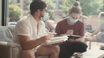 Men wearing face masks reading and discussing scripture in a coffee shop 