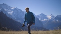 A young man walking towards and past camera in a mountain field with epic mountains in background