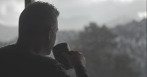 man drinking coffee looking out a window 