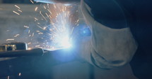 Welder welding metal parts in a workshop wearing a mask and protective gear