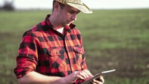 Young farmer standing in a wheat field and looking at tablet.