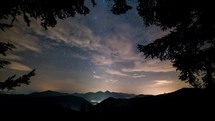 Beautiful forest view of starry night sky with milky way galaxy and clouds moving over alps mountains nature Time lapse
