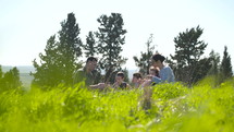 A family having a picnic outdoors on a green hill in the sun.