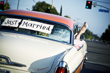 Bride and groom in classic car with "Just Married" in back window brides foot hanging out window