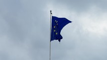 European Union Flag with golden stars flutters in the wind against a cloudy sky