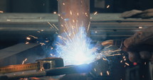 Welder welding metal parts in a workshop wearing a mask and protective gear