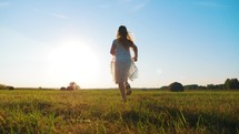 Happy childhood. Cheerful girl are running in the green meadow. Back view of girl running on flower meadow at evening twilight. Teen girl running on meadow with sunset. Happy family concept.