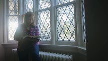 a woman praying at a window and reading a Bible 