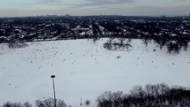 Aerial orbit shot of Riverdale Park East in dynamic Toronto eastside neighborhood on a cold winter day. Aircraft flying over Don Valley Parkway while people are playing with snow in the park.