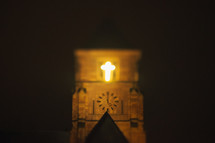 glowing cross on a church bell tower at night 