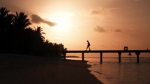 Silhouette of a woman walking on a pear at the beach at sunset