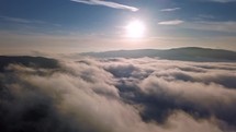 Fly above low clouds in foggy nature landscape outdoor in sunny autumn day with sun on blue sky Aerial view
