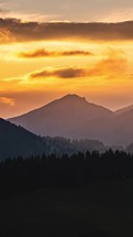 Vertical video of golden sky with fast moving clouds above forest mountains landscape timelapse
