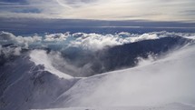 View from snowy alpine mountains in winter above clouds.
