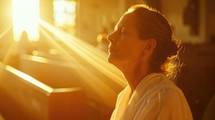 Sunlit prayer. Older woman praying in the church in the sunbeams shining through the window.